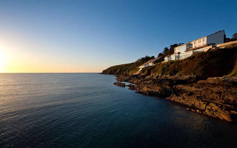 Seaview of Cliff House Hotel built into the cliff-face with the sun rising over Ardmore bay, ideal for Valentine's Day Celebrations and a great coastal stay with a winter sale
